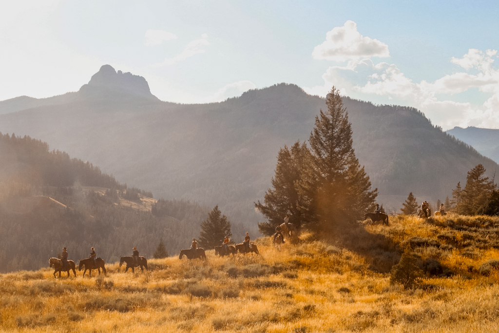 A cowboy leads a long line of riders in front of the majesty of Cody Peak.